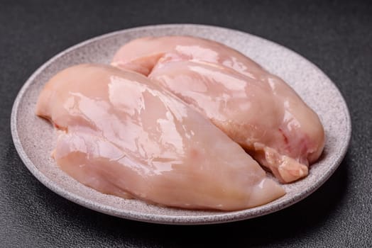 Raw chicken or turkey fillet with salt, spices and herbs on a dark concrete background