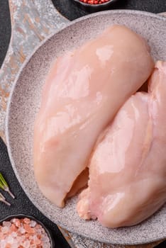 Raw chicken or turkey fillet with salt, spices and herbs on a dark concrete background