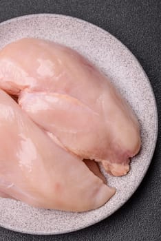 Raw chicken or turkey fillet with salt, spices and herbs on a dark concrete background