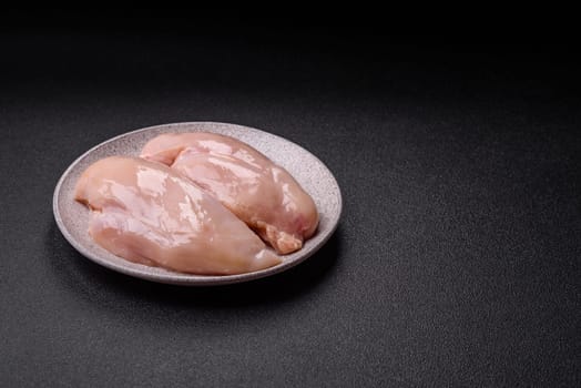 Raw chicken or turkey fillet with salt, spices and herbs on a dark concrete background