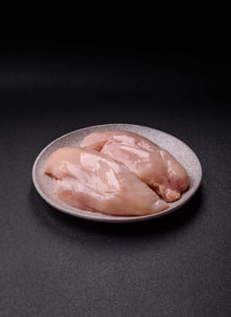 Raw chicken or turkey fillet with salt, spices and herbs on a dark concrete background
