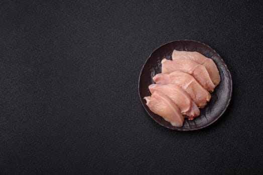 Raw chicken or turkey fillet cut into slices with salt, spices and herbs on a dark concrete background