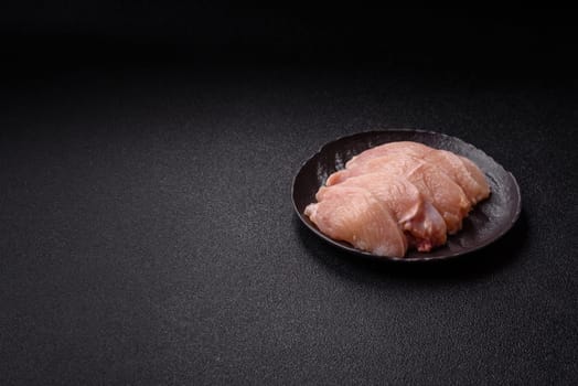 Raw chicken or turkey fillet cut into slices with salt, spices and herbs on a dark concrete background