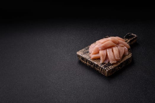 Raw chicken or turkey fillet cut into slices with salt, spices and herbs on a dark concrete background