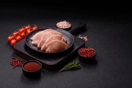 Raw chicken or turkey fillet cut into slices with salt, spices and herbs on a dark concrete background