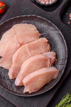 Raw chicken or turkey fillet cut into slices with salt, spices and herbs on a dark concrete background