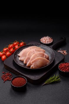 Raw chicken or turkey fillet cut into slices with salt, spices and herbs on a dark concrete background