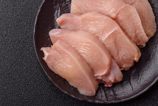 Raw chicken or turkey fillet cut into slices with salt, spices and herbs on a dark concrete background