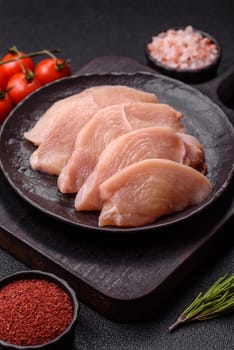 Raw chicken or turkey fillet cut into slices with salt, spices and herbs on a dark concrete background