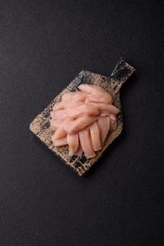 Raw chicken or turkey fillet cut into slices with salt, spices and herbs on a dark concrete background