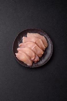 Raw chicken or turkey fillet cut into slices with salt, spices and herbs on a dark concrete background