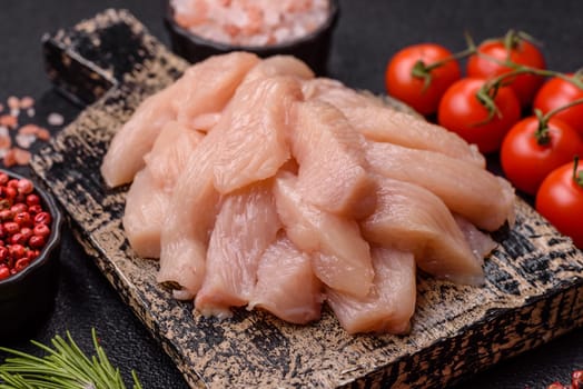 Raw chicken or turkey fillet cut into slices with salt, spices and herbs on a dark concrete background