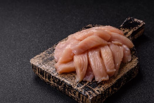 Raw chicken or turkey fillet cut into slices with salt, spices and herbs on a dark concrete background