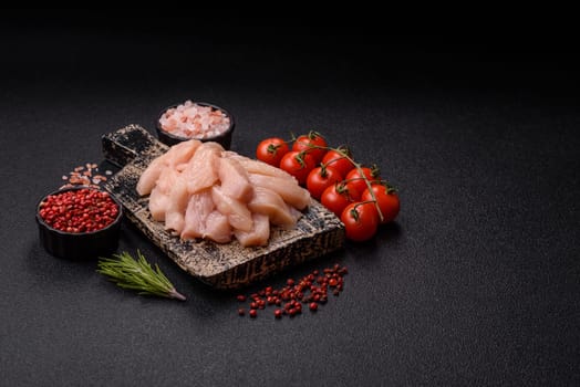Raw chicken or turkey fillet cut into slices with salt, spices and herbs on a dark concrete background