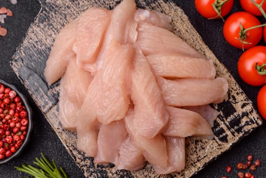 Raw chicken or turkey fillet cut into slices with salt, spices and herbs on a dark concrete background