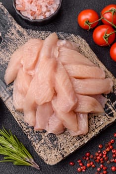 Raw chicken or turkey fillet cut into slices with salt, spices and herbs on a dark concrete background