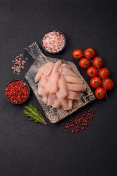 Raw chicken or turkey fillet cut into slices with salt, spices and herbs on a dark concrete background