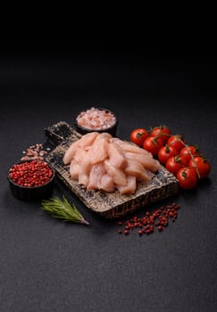 Raw chicken or turkey fillet cut into slices with salt, spices and herbs on a dark concrete background