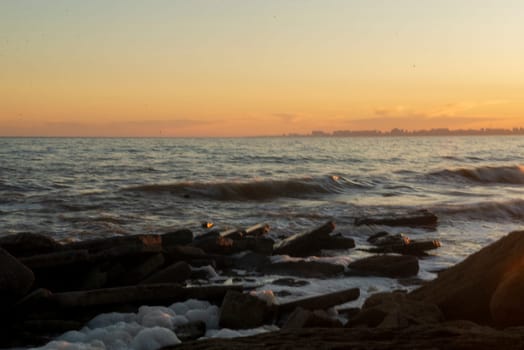 Picturesque sunset over stormy sea. White foam from the waves is visible on the beach. Sunset sea of ​​rich shades with orange color.