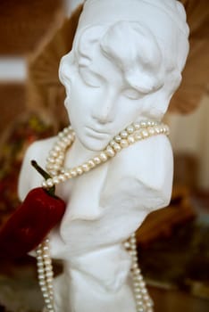 bust of a plaster girl with pearls and red hot peppers on her neck. High quality photo
