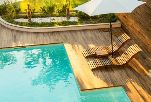 Stylish poolside wooden deck with curved lounge chairs, umbrella, and turquoise pool in a serene backyard