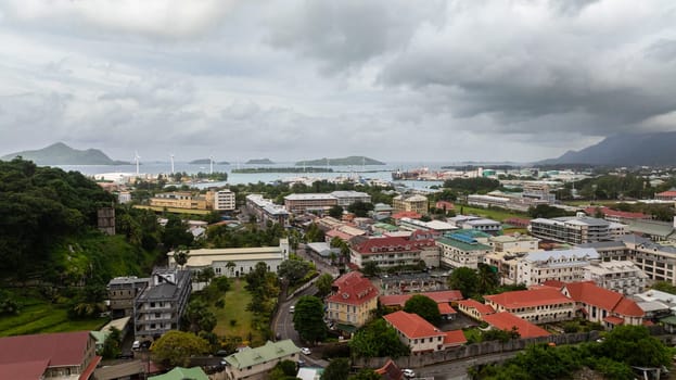 An aerial view reveals a port city with wind turbines, surrounded by turquoise waters and scattered islands in the background. Victoria city. Mahe, Seychelles.