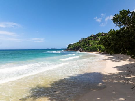 White sands stretch along the beach, meeting clear, calm waters and lush greenery. Seychelles, Mahe. Anse Louis beach.