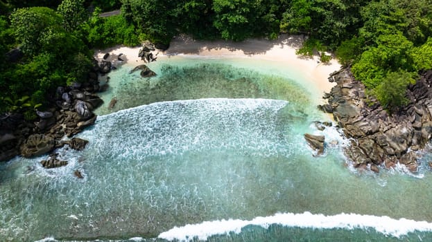 Hidden sandy beach framed by vibrant vegetation and rugged stones. Seychelles, Mahe.