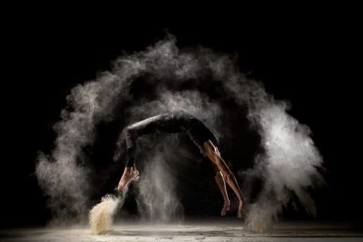 Male gymnast jumping in white dust cloud profile view in the dark room