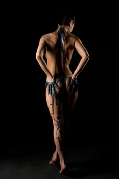 Slim nude woman in gray paint cropped rearview in the dark room