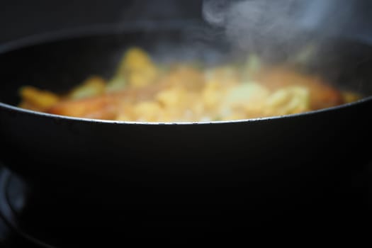 Steam rises from a savory dish being cooked in a black frying pan.