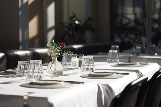 Tables are neatly arranged with plates and glasses, illuminated by sunlight.