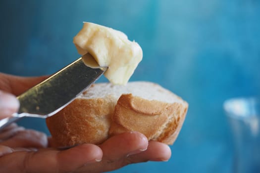 A hand applies soft butter on a slice of bread against a blue background.