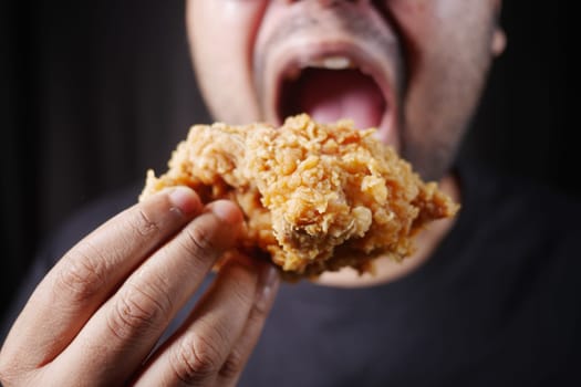 A person excitedly bites into a big piece of fried chicken.