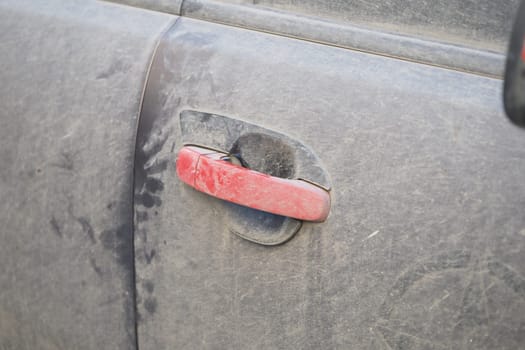 A dusty car door handle shows signs of outdoor exploration and use.