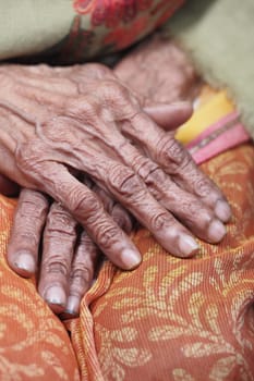 Elderly hands with intricate wrinkles resting on colorful cloth.
