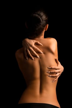 Girl topless embracing herself cropped rearview against black background