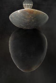 Reflection on a black surface of Old ancient worn vintage spoon in close up an oval is shaped like an egg. Curve details of Black metal vintage spoon in dark tone, Highlighting its texture and design, use it as your Space for text, Design, Wallpaper and Poster, Selective focus.