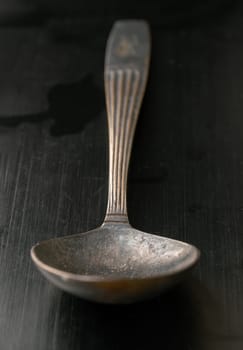 Perspective surface view of Ancient vintage spoon isolated on black background. Close-up of Black worn metal vintage spoon in dark tone, Highlighting its texture and design, use it as your Space for text, Design, Wallpaper and Poster, Selective focus.