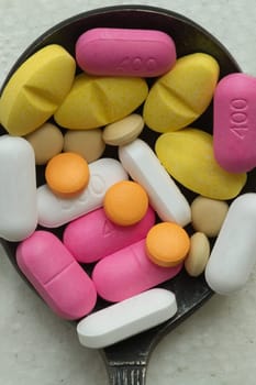 Top down view close up of A lot of pills of different colors and shapes stacked together on metal spoon with white background. Concept of medication treatment and Health care, use it as your Space for text, Design, Wallpaper and Poster, Selective focus.