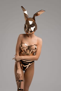Slim girl in blsm gold lingerie and rabbit mask shot against gray background