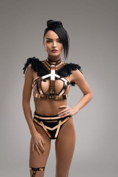 beautiful brunette in bdsm style gold and metal lingerie cropped view against gray background