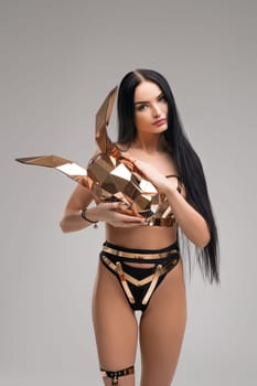 Slim brunette in bdsm style gold and metal underwear cropped view against gray background