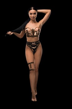 Slim brunette in bdsm style gold and metal lingerie full-length view against black background