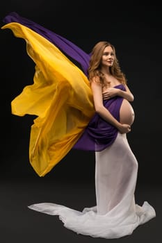 Pregnant woman with long locks wrapped in cloth against black background view