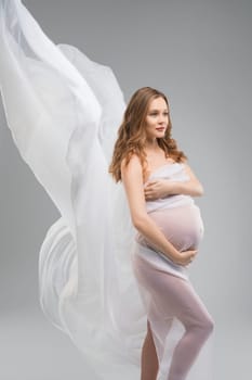 Pregnant woman with long locks against gray background view