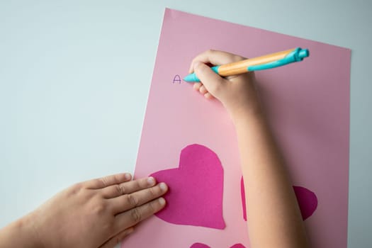 Child making heart shaped card with pink paper and letters.