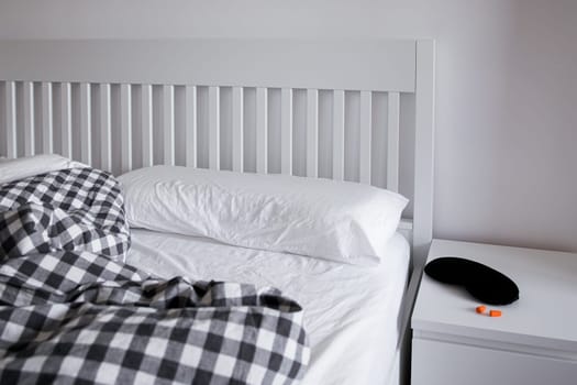 Cozy white bedroom with checkered blanket and black sleep mask on nightstand.