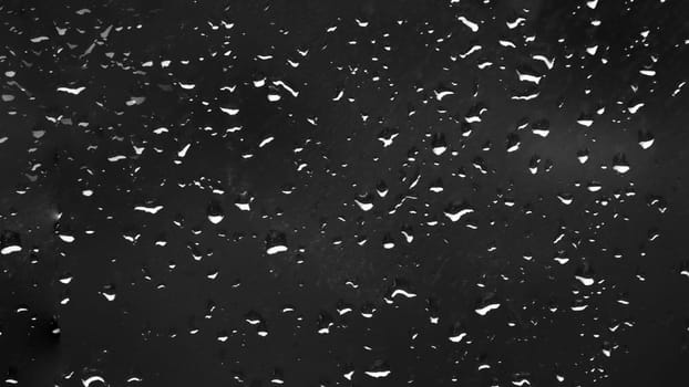 Small drops of water on the window at night, water on glass after rain.