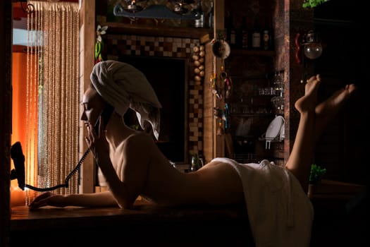 Nude girl her head wrapped in a towel lying on the table and speaking over the phone in sauna view